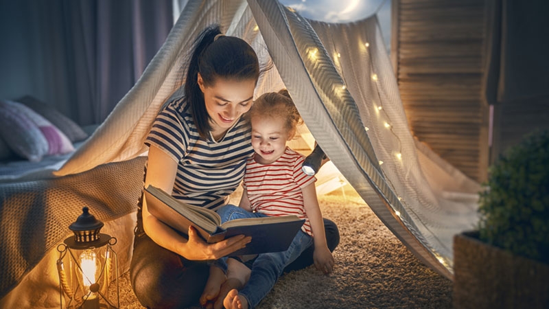 At home, a mother and her daughter are reading a book. 